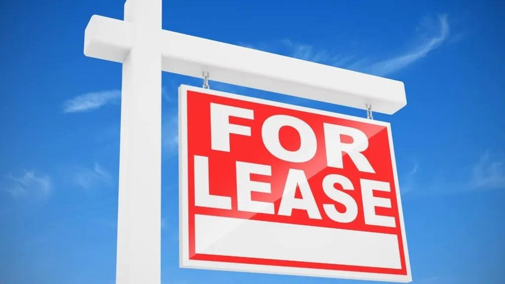 Red and white For Lease sign hanging from a white post against a blue sky