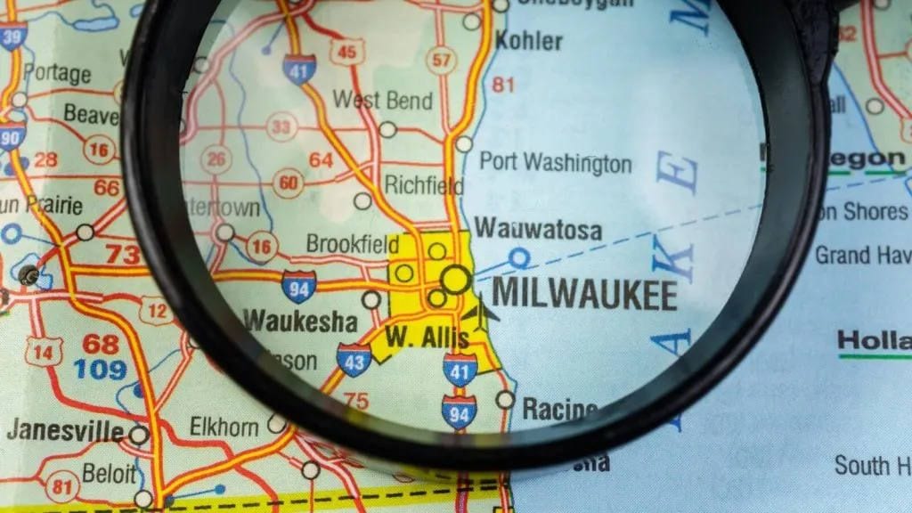 Magnifying glass over a road map centered on Milwaukee and nearby cities like Waukesha and Wauwatosa