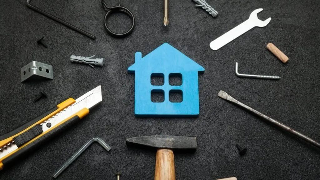 Blue wooden house cutout surrounded by hammer, wrench, screwdriver and other repair tools
