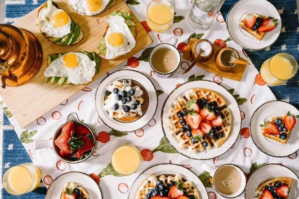 Brunch table spread with avocado toast and eggs, waffles with berries, coffee and orange juice