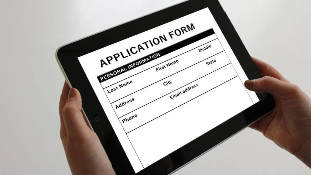 Hands holding a tablet showing a rental application form with personal information fields