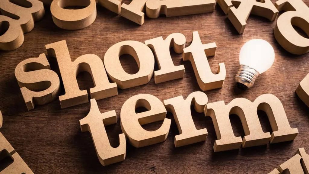 Wooden letters spelling short term next to a glowing light bulb