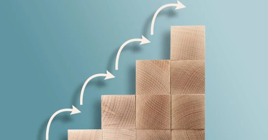 Wooden blocks rising like stairs with arrows showing step-by-step progress