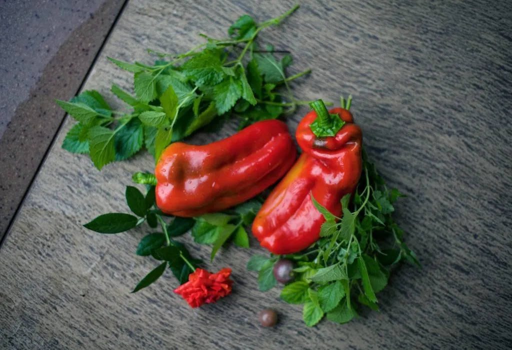 Two red peppers with fresh herbs on a wooden surface