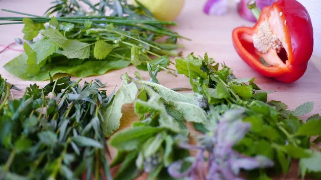 Fresh garden herbs and a sliced red pepper on a wooden cutting board